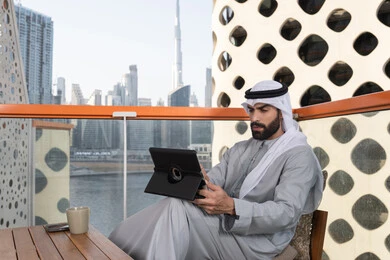 تصفح مواقع التواصل الاجتماعي، إدارة شؤون الأعمال وتنظيمها عبر جهاز التابلت، دمج العمل مع التقنية والتكنولوجيا ، شاب عربي خليجي إماراتي يرتدي الكندورة والغترة البيضاء يجلس في المقهى، قضاء وقت ممتع فى الخارج