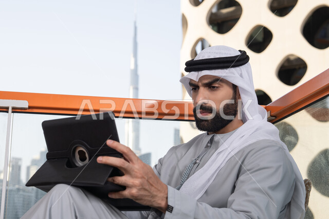 تبادل الأحاديث والتواصل والأخبار مع الأهل والأصدقاء، استخدم جهاز التابلت لانجاز المشاريع والمهام،  مفهوم التكنولوجيا وإستخدام تقنيات حديثة ، شاب عربي خليجي إماراتي يرتدي الكندورة والغترة البيضاء يجلس في المقهى، قضاء وقت ممتع فى الخارج