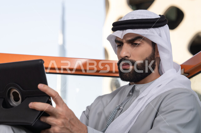 مفهوم التكنولوجيا وإستخدام تقنيات حديثة ،صورة مقربه لشاب عربي خليجي إماراتي يرتدي الكندورة والغترة البيضاء يجلس في المقهى، قضاء وقت ممتع فى الخارج ، اجراء مكالمه فيديو، استخدم جهاز التابلت لانجاز المشاريع والمهام