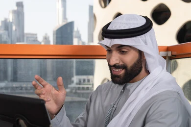 Integrating technology and tech into daily routines, expressions of happiness and joy, a close-up image of an Arab Gulf Emirati man wearing a kandura and ghutrah using a tablet in a high café overlooking the city.