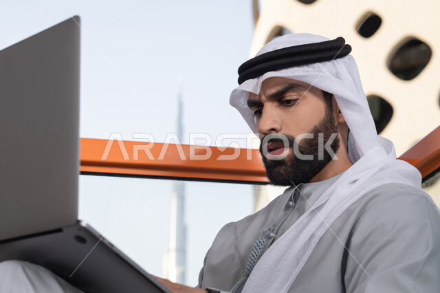 التواصل مع الأهل والاصدقاء عبر اللابتوب ، إنجاز مهام العمل عن بعد، إدارة شؤون الأعمال وتنظيمها ، استخدام جهاز تقني حديث ومتطور، رجل عربي خليجي اماراتي يرتدي الكندورة والغترة البيضاء يستخدم الحاسوب المحمول