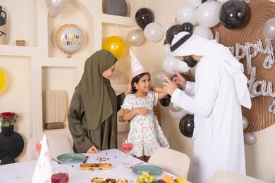 Joyful atmosphere for an Emirati family, happy holidays and occasions, strengthening family ties, feelings of love and tenderness in a happy family gathering, the concept of the importance of family, decoration, hanging balloons and celebration, gestures of happiness and pleasure, an Emirati Gulf Arab family celebrating their daughter's birthday, feelings of love and tenderness in a happy family gathering
