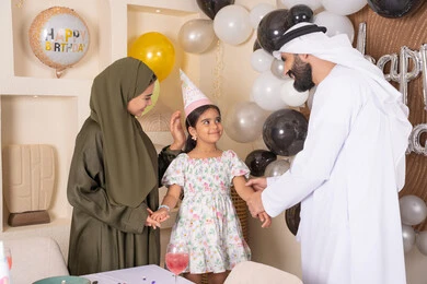 Feelings of love and tenderness in a happy family gathering, the concept of the importance of family, strengthening family ties, decorating and hanging balloons and celebration, gestures of happiness and pleasure, a joyful atmosphere for an Emirati family, happy holidays and occasions, an Arab Gulf Emirati family celebrating their daughter's birthday, feelings of love and tenderness in a happy family gathering