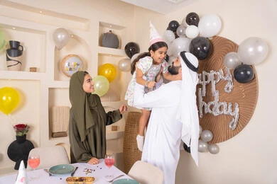 أجواء فرحة لأسرة اماراتية، اعياد ومناسبات سعيدة ، مفهوم الحب والالفه والموده، رجل اماراتي يحمل ابنته لاعلى بايماءات السعاده والسرور، عائله عربيه خليجيه اماراتية تحتفل بعيد ميلاد ابنتهم ، التزيين وتعليق البلالين والاحتفال، مشاعر الحب والحنان في اجتماع عائلي سعيد
