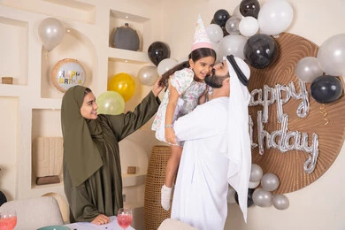 مفهوم الحب والالفه والموده، رجل اماراتي يحمل ابنته لاعلى بايماءات السعاده والسرور، عائله عربيه خليجيه اماراتية تحتفل بعيد ميلاد ابنتهم ، التزيين وتعليق البلالين والاحتفال، مشاعر الحب والحنان في اجتماع عائلي سعيد، أجواء فرحة لأسرة اماراتية، اعياد ومناسبات سعيدة