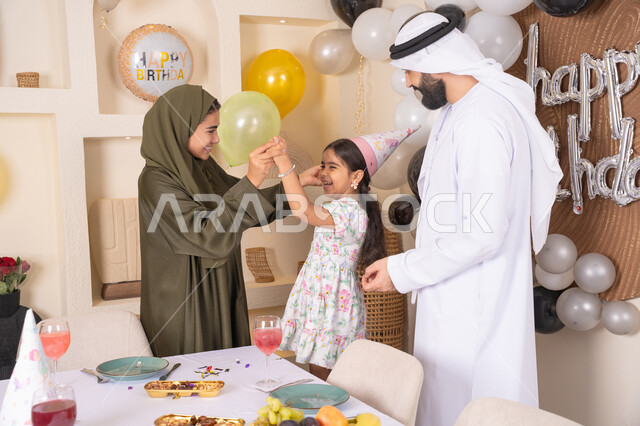 Gestures of happiness and joy, decoration, hanging balloons and celebration, an Emirati Gulf Arab family celebrating their daughter's birthday, feelings of love and tenderness in a happy family gathering, the concept of love, intimacy and affection, a joyful atmosphere for an Emirati family, happy holidays and occasions
