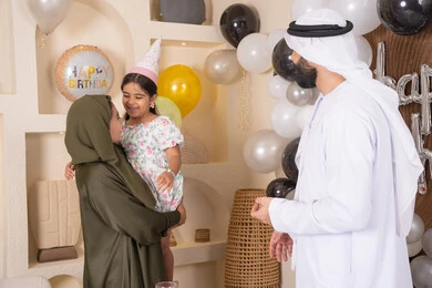 مشاعر الحب والحنان في اجتماع عائلي سعيد، اعياد ومناسبات سعيدة، مفهوم الحب والالفه والموده، عائله عربيه خليجيه اماراتية تحتفل بعيد ميلاد ابنتهم ، ام اماراتيه تحمل ابنتها لاعلى بتعابير البهجة، مشاركة لأجواء رائعة عائلية داخل المنزل، تعليق الزينة والبالونات الملونة ، ايماءات السعاده والسرور