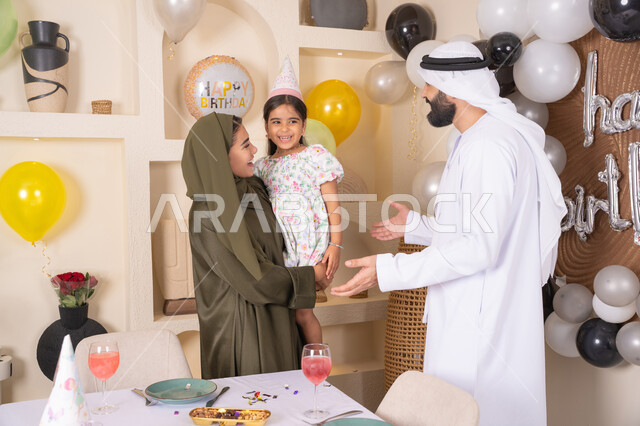 اعياد ومناسبات سعيدة، مفهوم الحب والالفه والموده، عائله عربيه خليجيه اماراتية تحتفل بعيد ميلاد ابنتهم ، ام اماراتيه تحمل ابنتها لاعلى بتعابير البهجة، مشاركة لأجواء رائعة عائلية داخل المنزل، تعليق الزينة والبالونات الملونة ، ايماءات السعاده والسرور ، مشاعر الحب والحنان في اجتماع عائلي سعيد