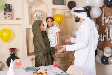 اعياد ومناسبات سعيدة، مفهوم الحب والالفه والموده، عائله عربيه خليجيه اماراتية تحتفل بعيد ميلاد ابنتهم ، ام اماراتيه تحمل ابنتها لاعلى بتعابير البهجة، مشاركة لأجواء رائعة عائلية داخل المنزل، تعليق الزينة والبالونات الملونة ، ايماءات السعاده والسرور ، مشاعر الحب والحنان في اجتماع عائلي سعيد