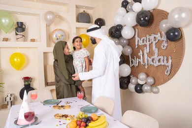 ام اماراتيه تحمل ابنتها لاعلى بتعابير البهجة، مشاركة لأجواء رائعة عائلية داخل المنزل، تعليق الزينة والبالونات الملونة ، ايماءات السعاده والسرور ، اعياد ومناسبات سعيدة،  مشاعر الحب والحنان في اجتماع عائلي سعيد، مفهوم الحب والالفه والموده، عائله عربيه خليجيه اماراتية تحتفل بعيد ميلاد ابنتهم
