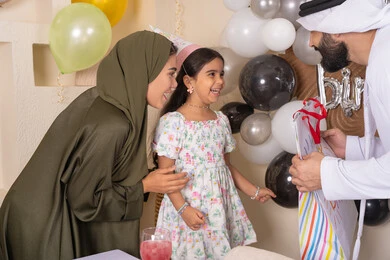 تعليق الزينة والبالونات الملونة ،  مشاركة لأجواء رائعة عائلية داخل المنزل، ايماءات السعاده والسرور ، رجل اماراتي يقوم بتقديم الهديه ويفاجئ ابنته ،اعياد ومناسبات سعيدة، مفهوم الحب والالفه والموده، عائله عربيه خليجيه اماراتية تحتفل بعيد ميلاد ابنتهم