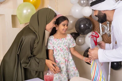 مشاركة لأجواء رائعة عائلية داخل المنزل، ايماءات السعاده والسرور ، رجل اماراتي يقوم بتقديم الهديه ويفاجئ ابنته ،تعليق الزينة والبالونات الملونة ، اعياد ومناسبات سعيدة، مفهوم الحب والالفه والموده، عائله عربيه خليجيه اماراتية تحتفل بعيد ميلاد ابنتهم
