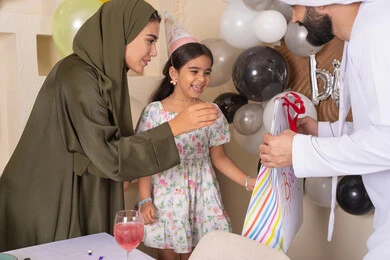 ايماءات السعاده والسرور ، رجل اماراتي يقوم بتقديم الهديه ويفاجئ ابنته ،تعليق الزينة والبالونات الملونة ، اعياد ومناسبات سعيدة، مفهوم الحب والالفه والموده، عائله عربيه خليجيه اماراتية تحتفل بعيد ميلاد ابنتهم ، مشاركة لأجواء رائعة عائلية داخل المنزل