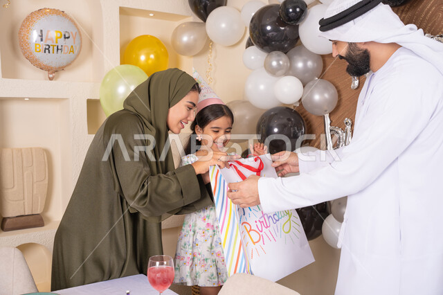 رجل اماراتي يقوم بتقديم الهديه ويفاجئ ابنته ،تعليق الزينة والبالونات الملونة ، اعياد ومناسبات سعيدة، مفهوم الحب والالفه والموده، تعابير المفاجأه والسعادة و السرور، عائله عربيه خليجيه اماراتية تحتفل بعيد ميلاد ابنتهم ، مشاركة لأجواء رائعة عائلية داخل المنزل