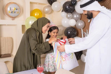 رجل اماراتي يقوم بتقديم الهديه ويفاجئ ابنته ،تعليق الزينة والبالونات الملونة ، اعياد ومناسبات سعيدة، مفهوم الحب والالفه والموده، تعابير المفاجأه والسعادة و السرور، عائله عربيه خليجيه اماراتية تحتفل بعيد ميلاد ابنتهم ، مشاركة لأجواء رائعة عائلية داخل المنزل