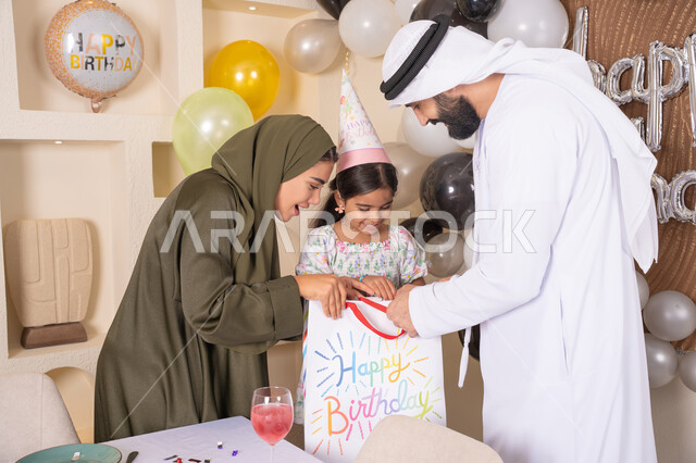 تعليق الزينة والبالونات الملونة ، اعياد ومناسبات سعيدة، مفهوم الحب والالفه والموده، تعابير المفاجأه والسعادة و السرور، عائله عربيه خليجيه اماراتية تحتفل بعيد ميلاد ابنتهم وتقدم الهدايا ،تقديم الهدايا والمفاجآت للأطفال، مشاركة لأجواء رائعة عائلية داخل المنزل