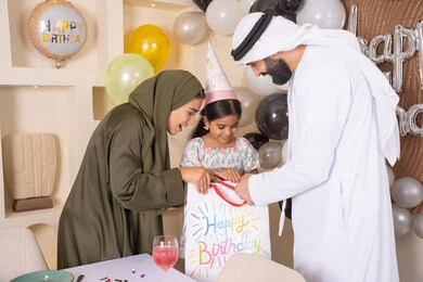 تعليق الزينة والبالونات الملونة ، اعياد ومناسبات سعيدة، مفهوم الحب والالفه والموده، تعابير المفاجأه والسعادة و السرور، عائله عربيه خليجيه اماراتية تحتفل بعيد ميلاد ابنتهم وتقدم الهدايا ،تقديم الهدايا والمفاجآت للأطفال، مشاركة لأجواء رائعة عائلية داخل المنزل