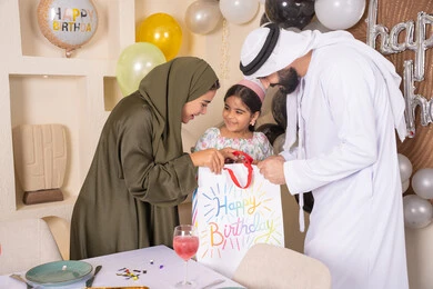 مفهوم الحب والالفه والموده، تعابير المفاجأه والسعادة و السرور، عائله عربيه خليجيه اماراتية تحتفل بعيد ميلاد ابنتهم وتقدم الهدايا ،اعياد ومناسبات سعيدة، تقديم الهدايا والمفاجآت للأطفال، مشاركة لأجواء رائعة عائلية داخل المنزل، تعليق الزينة والبالونات الملونة