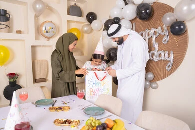 عائله عربيه خليجيه اماراتية تحتفل بعيد ميلاد ابنتهم وتقدم الهدايا ،اعياد ومناسبات سعيدة، تقديم الهدايا والمفاجآت للأطفال، مفهوم الحب والالفه والموده، مشاركة لأجواء رائعة عائلية داخل المنزل، تعليق الزينة والبالونات الملونة، تعابير المفاجأه والسعادة و السرور
