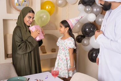 ام اماراتيه تقوم بتقديم الهديه لابنتها ، تعابير المفاجأه والسعادة و السرور، عائله عربيه خليجيه اماراتية تحتفل بعيد ميلاد ابنتهم ،اعياد ومناسبات سعيدة، تقديم الهدايا والمفاجآت للأطفال، مفهوم الحب والالفه والموده،مشاركة لأجواء رائعة عائلية داخل المنزل، تعليق الزينة والبالونات الملونة