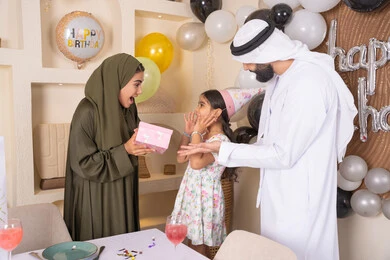 تعابير المفاجأه والسعادة و السرور، عائله عربيه خليجيه اماراتية تحتفل بعيد ميلاد ابنتهم ،اعياد ومناسبات سعيدة، تقديم الهدايا والمفاجآت للأطفال، مفهوم الحب والالفه والموده،مشاركة لأجواء رائعة عائلية داخل المنزل، تعليق الزينة والبالونات الملونة، ام اماراتيه تقوم بتقديم الهديه لابنتها