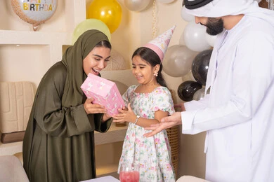 عائله عربيه خليجيه اماراتية تحتفل بعيد ميلاد ابنتهم ،اعياد ومناسبات سعيدة، تقديم الهدايا والمفاجآت للأطفال، مفهوم الحب والالفه والموده،مشاركة لأجواء رائعة عائلية داخل المنزل،  ايماءات السعادة و السرور،  تعليق الزينة والبالونات الملونة، ام اماراتيه تقوم بتقديم الهديه لابنتها