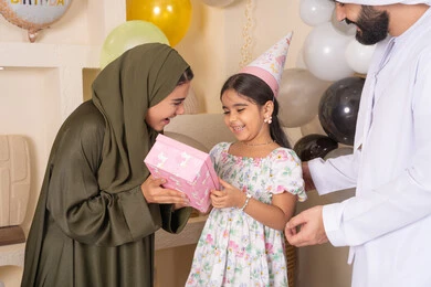 تقديم الهدايا والمفاجآت للأطفال، مفهوم الحب والالفه والموده،مشاركة لأجواء رائعة عائلية داخل المنزل،  ايماءات السعادة و السرور، عائله عربيه خليجيه اماراتية تحتفل بعيد ميلاد ابنتهم ،اعياد ومناسبات سعيدة، تعليق الزينة والبالونات الملونة، ام اماراتيه تقوم بتقديم الهديه لابنتها