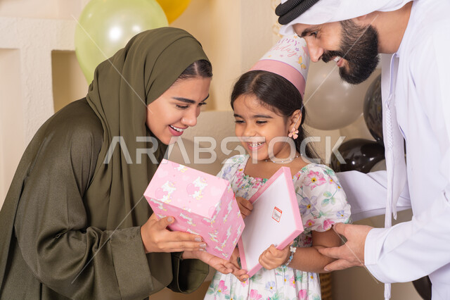 مفهوم الحب والالفه والموده، تقديم الهدايا والمفاجآت للأطفال، مشاركة لأجواء رائعة عائلية داخل المنزل،  ايماءات السعادة و السرور، عائله عربيه خليجيه اماراتية تحتفل بعيد ميلاد ابنتهم ،اعياد ومناسبات سعيدة، تعليق الزينة والبالونات الملونة، ام اماراتيه تقوم بتقديم الهديه لابنتها