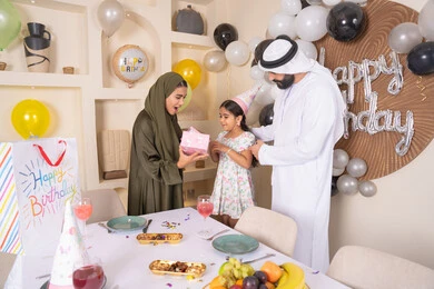 عائله عربيه خليجيه اماراتية تحتفل بعيد ميلاد ابنتهم ،اعياد ومناسبات سعيدة، ايماءات السعادة و السرور، مشاركة لأجواء رائعة عائلية داخل المنزل، تعليق الزينة والبالونات الملونة، ام اماراتيه تقوم بتقديم الهديه لابنتها ،مفهوم الحب والالفه والموده، تقديم الهدايا والمفاجآت للأطفال