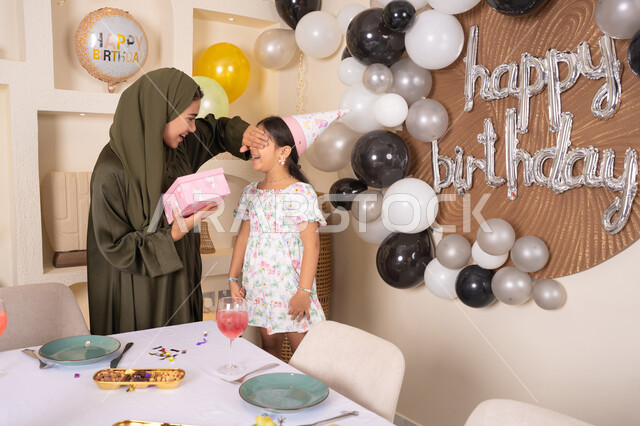 اعياد ومناسبات سعيدة، ايماءات السعادة و السرور، مشاركة لأجواء رائعة عائلية داخل المنزل،عائله عربيه خليجيه اماراتية تحتفل بعيد ميلاد ابنتهم ، تعليق الزينة والبالونات الملونة، ام اماراتيه تقوم بتقديم الهديه لابنتها ،مفهوم الحب والالفه والموده، تقديم الهدايا والمفاجآت للأطفال