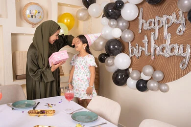 اعياد ومناسبات سعيدة، ايماءات السعادة و السرور، مشاركة لأجواء رائعة عائلية داخل المنزل،عائله عربيه خليجيه اماراتية تحتفل بعيد ميلاد ابنتهم ، تعليق الزينة والبالونات الملونة، ام اماراتيه تقوم بتقديم الهديه لابنتها ،مفهوم الحب والالفه والموده، تقديم الهدايا والمفاجآت للأطفال