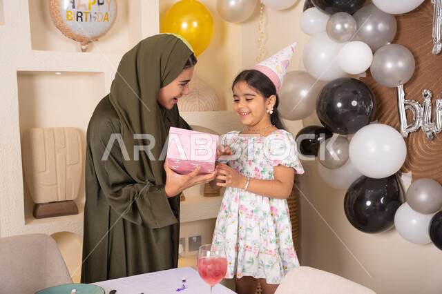 ايماءات السعادة و السرور، مشاركة لأجواء رائعة عائلية داخل المنزل،عائله عربيه خليجيه اماراتية تحتفل بعيد ميلاد ابنتهم ، تعليق الزينة والبالونات الملونة، ام اماراتيه تقوم بتقديم الهديه لابنتها ،مفهوم الحب والالفه والموده، تقديم الهدايا والمفاجآت للأطفال، اعياد ومناسبات سعيدة