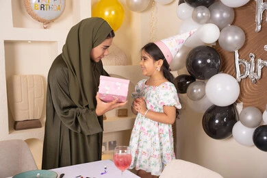 مشاركة لأجواء رائعة عائلية داخل المنزل،عائله عربيه خليجيه اماراتية تحتفل بعيد ميلاد ابنتهم ، تعليق الزينة والبالونات الملونة، ام اماراتيه تقوم بتقديم الهديه لابنتها ،مفهوم الحب والالفه والموده، تقديم الهدايا والمفاجآت للأطفال، اعياد ومناسبات سعيدة،ايماءات السعادة و السرور