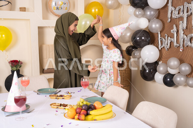 مفهوم الحب والالفه والموده، تقديم الهدايا والمفاجآت للأطفال، ام اماراتيه تحتفل بابنتها ، اعياد ومناسبات سعيدة، تعليق الزينة والبالونات الملونة، ايماءات السعادة و السرور،  مشاركة لأجواء رائعة عائلية داخل المنزل،عائله عربيه خليجيه اماراتية تقوم بالاحتفال بعيد ميلاد ابنتهم