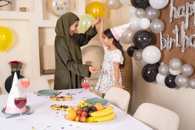 مفهوم الحب والالفه والموده، تقديم الهدايا والمفاجآت للأطفال، ام اماراتيه تحتفل بابنتها ، اعياد ومناسبات سعيدة، تعليق الزينة والبالونات الملونة، ايماءات السعادة و السرور،  مشاركة لأجواء رائعة عائلية داخل المنزل،عائله عربيه خليجيه اماراتية تقوم بالاحتفال بعيد ميلاد ابنتهم