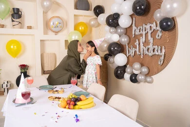 ام اماراتيه تقوم بتقبيل ابنتها ،مفهوم الحب والالفه والموده، تقديم الهدايا والمفاجآت للأطفال، اعياد ومناسبات سعيدة، تعليق الزينة والبالونات الملونة، ايماءات السعادة و السرور،  مشاركة لأجواء رائعة عائلية داخل المنزل،عائله عربيه خليجيه اماراتية تحتفل بعيد ميلاد ابنتهم