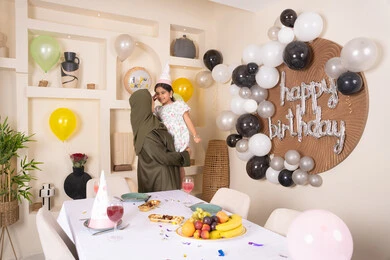 تقديم الهدايا والمفاجآت للأطفال، ام عربية خليجية تحمل ابنتها  للاعلى ، اعياد ومناسبات سعيدة، تعليق الزينة والبالونات الملونة، ايماءات السعادة و السرور، عائله عربيه خليجيه اماراتية تقوم بالاحتفال بعيد ميلاد ابنتهم