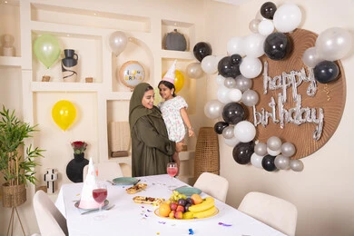 ام عربية خليجية تحمل ابنتها  للاعلى ، اعياد ومناسبات سعيدة، تعليق الزينة والبالونات الملونة، ايماءات السعادة و السرور، تقديم الهدايا والمفاجآت للأطفال، عائله عربيه خليجيه اماراتية تقوم بالاحتفال بعيد ميلاد ابنتهم