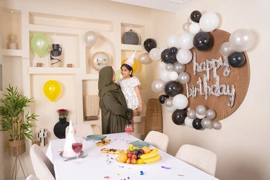 اعياد ومناسبات سعيدة، تعليق الزينة والبالونات الملونة، ايماءات السعادة و السرور، تقديم الهدايا والمفاجآت للأطفال، ام عربية خليجية تحمل ابنتها  للاعلى ، عائله عربيه خليجيه اماراتية تقوم بالاحتفال بعيد ميلاد ابنتهم