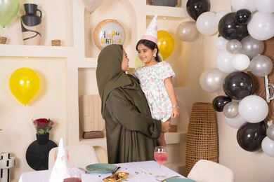 تعليق الزينة والبالونات الملونة، ايماءات السعادة و السرور، تقديم الهدايا والمفاجآت للأطفال، اعياد ومناسبات سعيدة، ام عربية خليجية تحمل ابنتها  للاعلى ، عائله عربيه خليجيه اماراتية تقوم بالاحتفال بعيد ميلاد ابنتهم