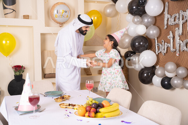 تعليق الزينة والبالونات الملونة، اب عربي خليجي يحتفل بابنته بايماءات السعادة و السرور، اعياد ومناسبات سعيدة، عائله عربيه خليجيه اماراتية تقوم بالاحتفال بعيد ميلاد ابنتهم ، تقديم الهدايا والمفاجآت للأطفال