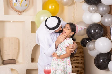 اب عربي خليجي يقوم بتقبيل ابنته بايماءات السعادة و السرور، اعياد ومناسبات سعيدة، تعليق الزينة والبالونات الملونة،  تقديم الهدايا والمفاجآت للأطفال، عائله عربيه خليجيه اماراتية تقوم بالاحتفال بعيد ميلاد ابنتهم