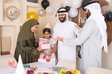 تعزيز الروابط العائلية والمحبة والمودة بين الأسرة،  مناسبات وأعياد سعيدة، عائلة عربية خليجية إماراتية تقوم بالاحتفال ، ام اماراتيه تقوم بتقديم الهديه لابنتها، إيماءات الفرح و السعادة، مشاعر الحب والحنان في اجتماع عائلي سعيد