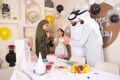 مشاعر الحب والحنان في اجتماع عائلي سعيد، إيماءات الفرح و السعادة، عائلة عربية خليجية إماراتية تحتفل بعيد ميلاد ابنتهم ، مشاركة وتقديم الهدايا بالمناسبات وأعياد الميلاد، أجواء أسرية مليئة بالألفة، بلالين وكعكة يوم الميلاد المزينة بالشموع