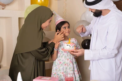 بلالين وكعكة يوم الميلاد المزينة بالشموع، أجواء أسرية مليئة بالألفة،مشاركة وتقديم الهدايا بالمناسبات وأعياد الميلاد، مشاعر الحب والحنان في اجتماع عائلي سعيد، إيماءات الفرح و السعادة، عائلة عربية خليجية إماراتية تحتفل بعيد ميلاد ابنتهم