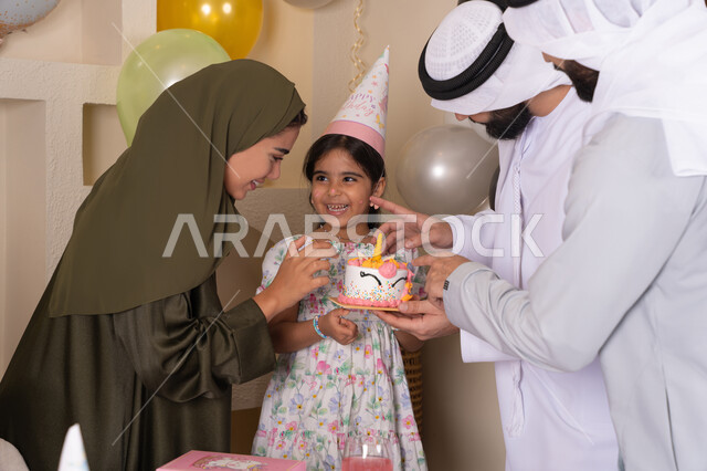 مشاعر الحب والحنان في اجتماع عائلي سعيد، إيماءات الفرح و السعادة، بلالين وكعكة يوم الميلاد المزينة بالشموع، أجواء أسرية مليئة بالألفة،مشاركة وتقديم الهدايا بالمناسبات وأعياد الميلاد،عائلة عربية خليجية إماراتية تحتفل بعيد ميلاد ابنتهم
