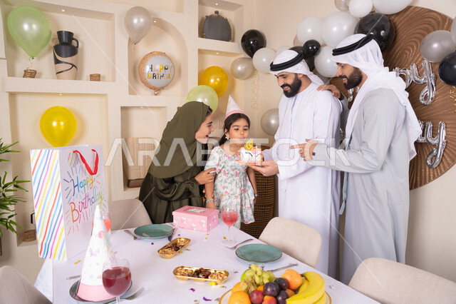 إيماءات الفرح و السعادة، مشاعر الحب والحنان في اجتماع عائلي سعيد، مشاركة وتقديم الهدايا بالمناسبات وأعياد الميلاد، أجواء أسرية مليئة بالألفة، بلالين وكعكة يوم الميلاد المزينة بالشموع، عائلة عربية خليجية إماراتية تقضي أوقات ممتعه في المنزل