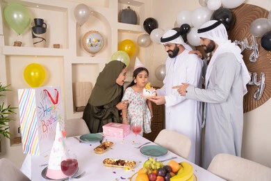 إيماءات الفرح و السعادة، مشاعر الحب والحنان في اجتماع عائلي سعيد، مشاركة وتقديم الهدايا بالمناسبات وأعياد الميلاد، أجواء أسرية مليئة بالألفة، بلالين وكعكة يوم الميلاد المزينة بالشموع، عائلة عربية خليجية إماراتية تقضي أوقات ممتعه في المنزل