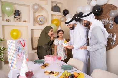 مشاركة وتقديم الهدايا بالمناسبات وأعياد الميلاد، أجواء أسرية مليئة بالألفة، بلالين وكعكة يوم الميلاد المزينة بالشموع، عائلة عربية خليجية إماراتية تقضي أوقات ممتعه في المنزل ، إيماءات الفرح و السعادة،  مشاعر الحب والحنان في اجتماع عائلي سعيد
