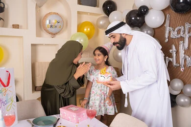 عائلة عربية خليجية إماراتية تقضي أوقات ممتعه في المنزل ، إيماءات الفرح و السعادة، مشاركة وتقديم الهدايا بالمناسبات وأعياد الميلاد، مشاعر الحب والحنان في اجتماع عائلي سعيد، أجواء أسرية مليئة بالألفة، بلالين وكعكة يوم الميلاد المزينة بالشموع